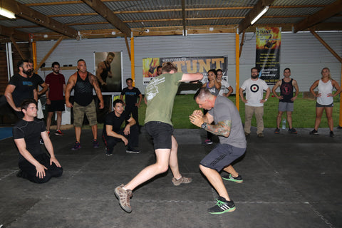 Two men participating in a stunt fighting brawl while others circle around. 