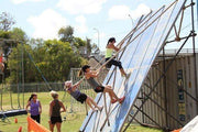 Three women climbing up a diagonal wall with a rope