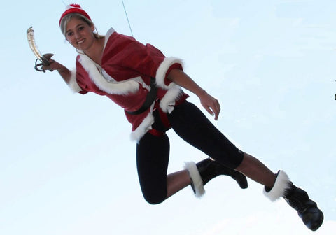 A girl in a Santa Claus outfit flying on wires with a sword. 